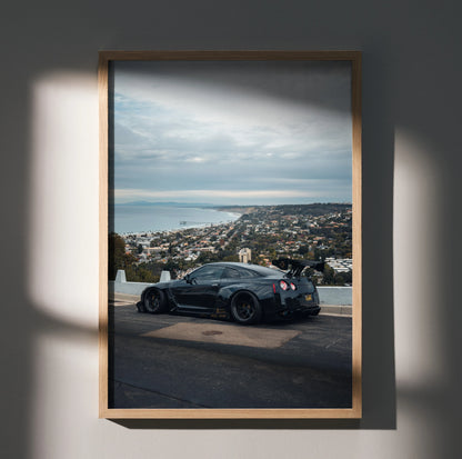 Nissan R35 GTR black sports car on coastal road poster wall art in wooden frame.