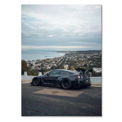 Sleek black Nissan R35 GTR parked overlooking coastal cityscape poster wall art.