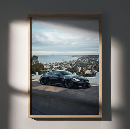 Nissan R35 GTR black sports car poster wall art with cityscape background in wooden frame.