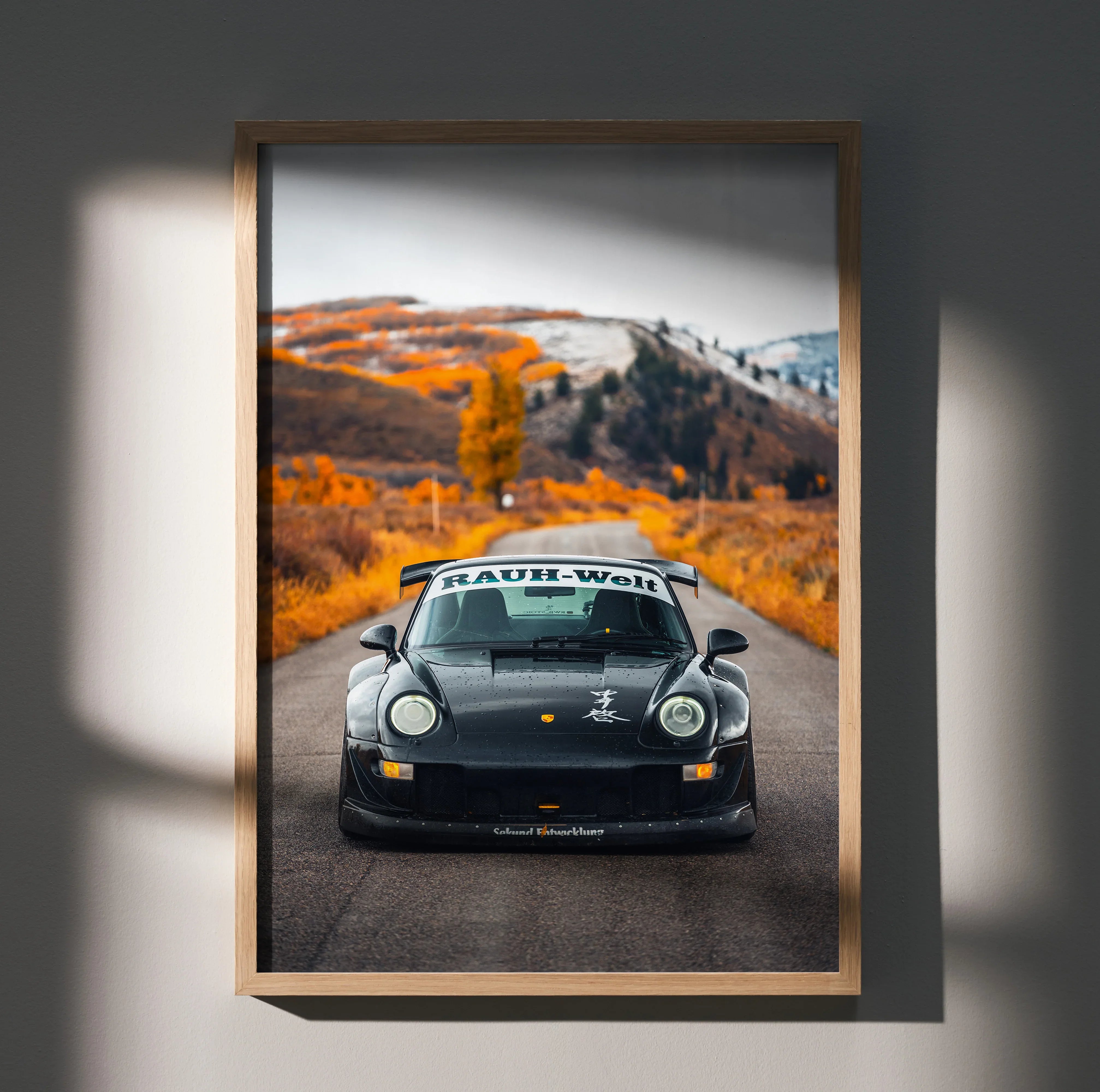 Black RWB Porsche 911 on autumn road with orange foliage poster wall art in wooden frame.