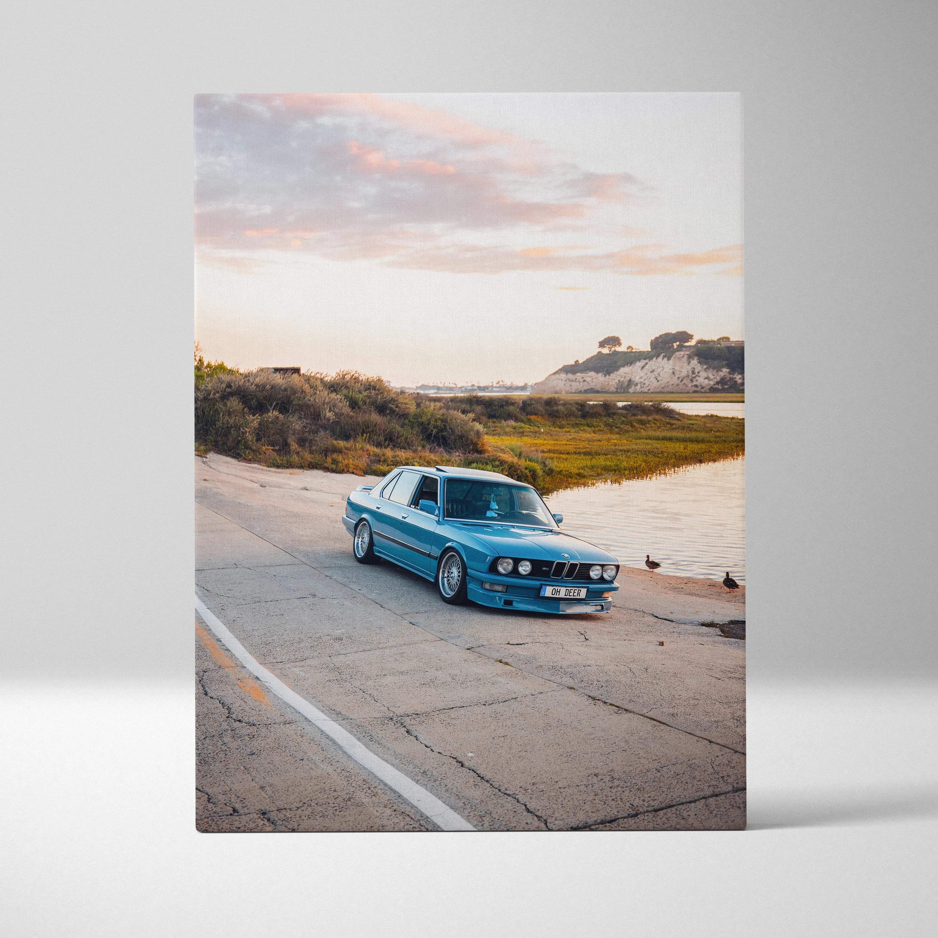 Blue BMW E28 5 Series on coastal road at sunset vertical canvas wall art.