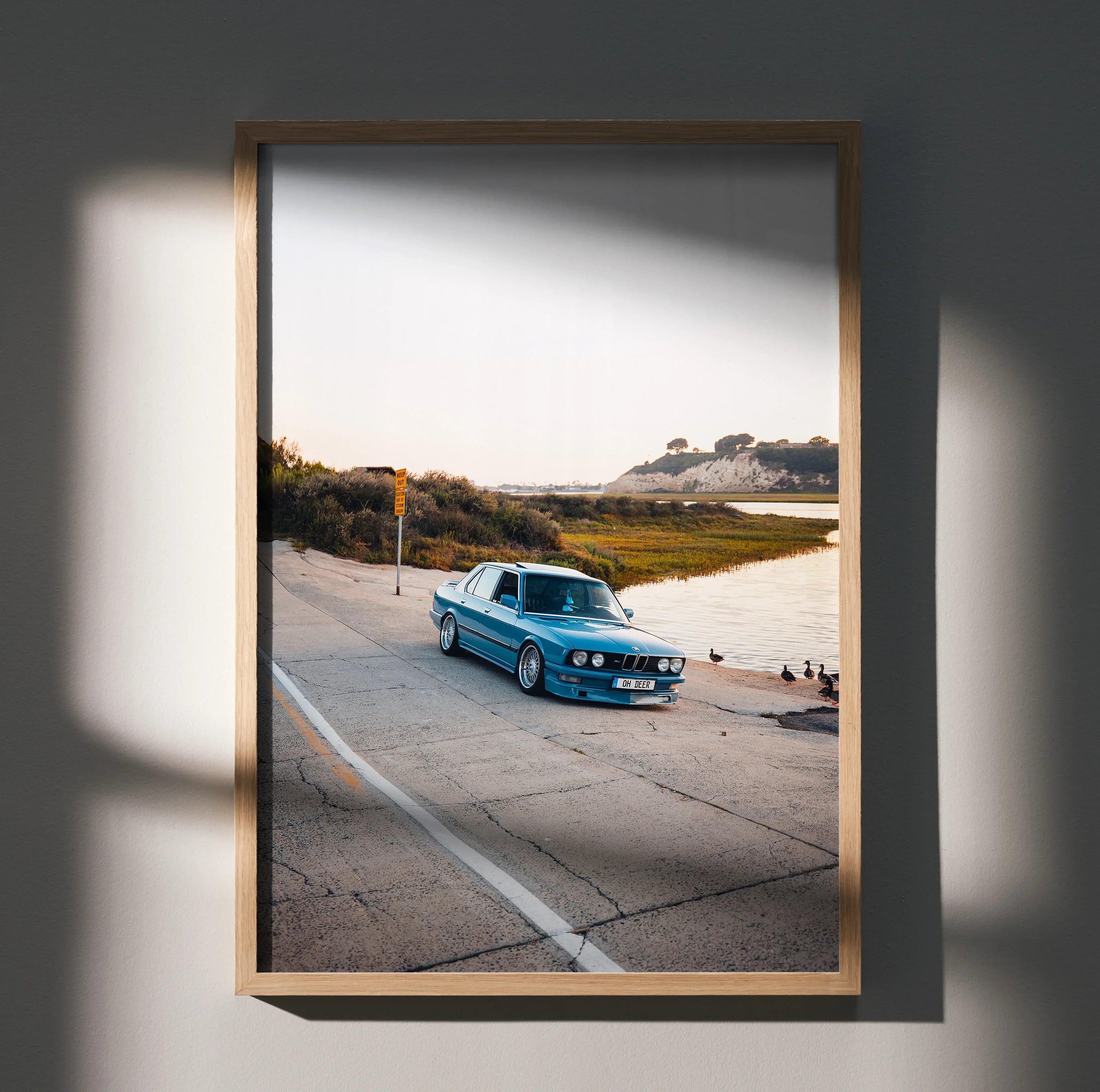 BMW E28 5 Series classic blue car on coastal road poster wall art in wooden frame.