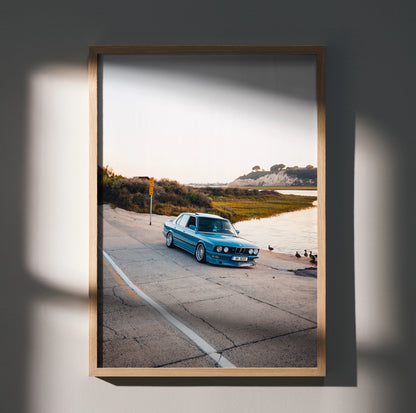 BMW E28 5 Series classic blue car on coastal road poster wall art in wooden frame.