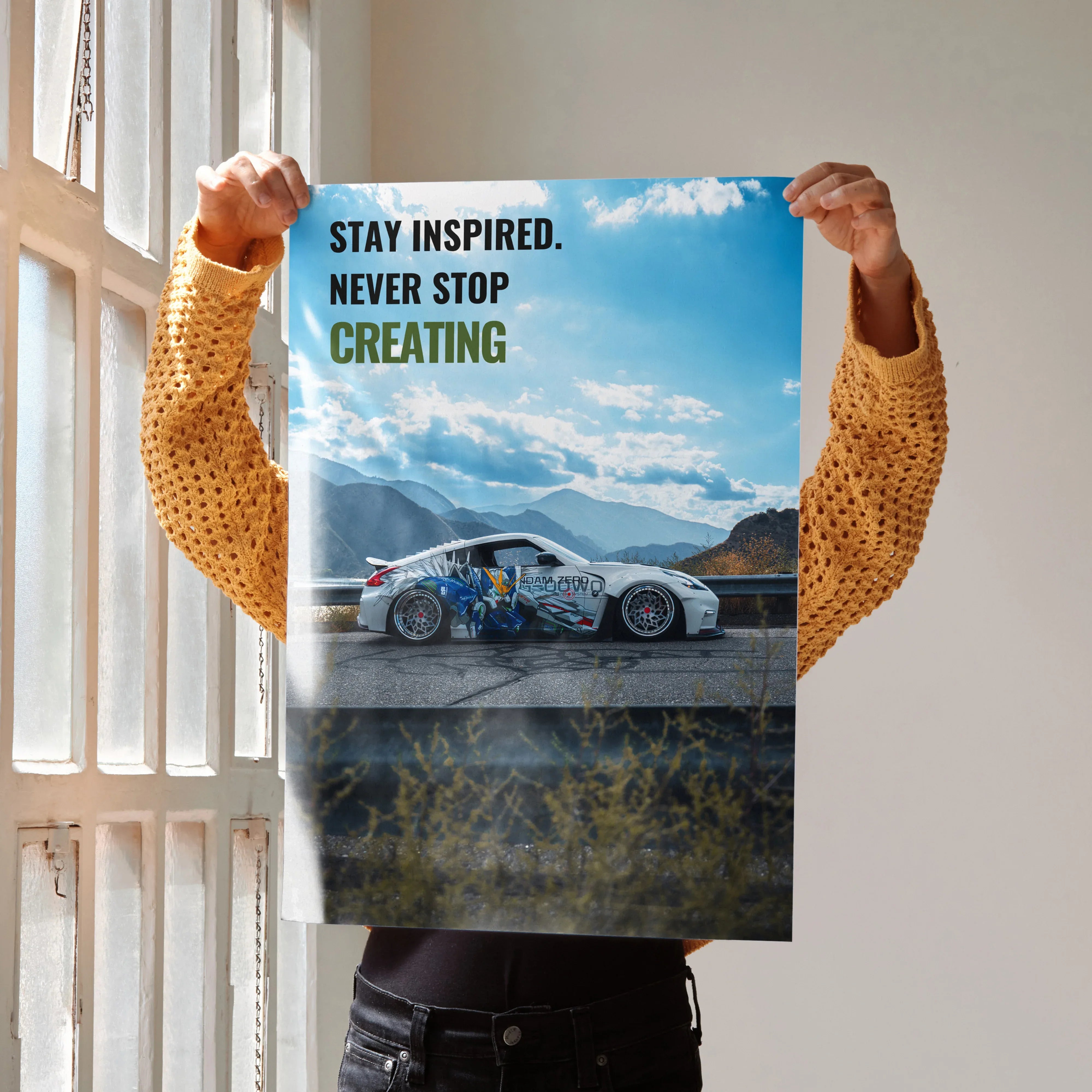 Motivational poster wall art with a Nissan 370z car and text "Stay Inspired. Never Stop Creating" against a sky background.