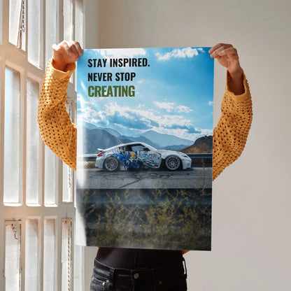 Motivational poster wall art with a Nissan 370z car and text "Stay Inspired. Never Stop Creating" against a sky background.