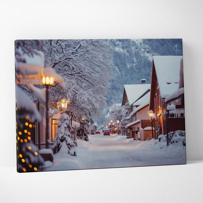 Canvas wall art depicting a snowy mountain town at dusk with warm street lamps and snow-covered buildings.