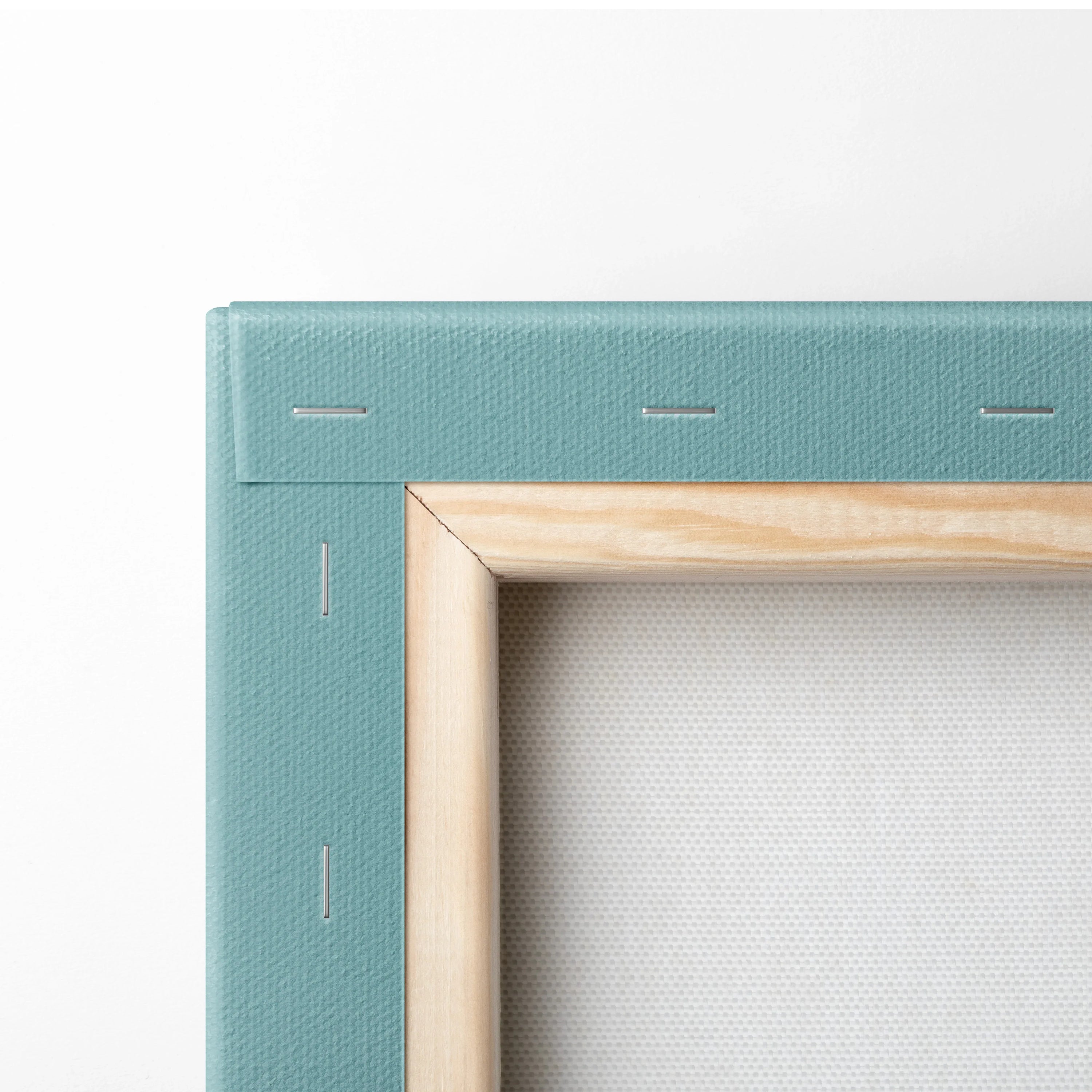 Close-up of canvas corner with light wood frame and teal fabric edge, showing stapled construction for wall art.