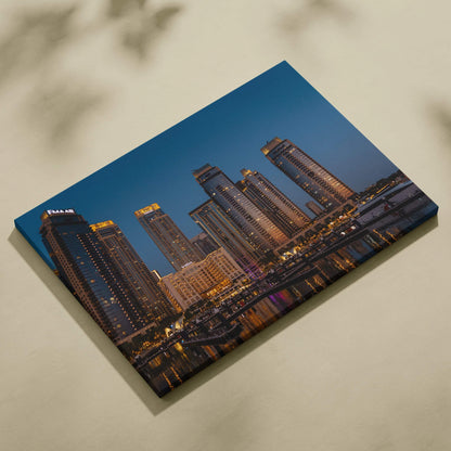 Canvas wall art featuring a digital print of illuminated modern skyscrapers at dusk against a deep blue sky.
