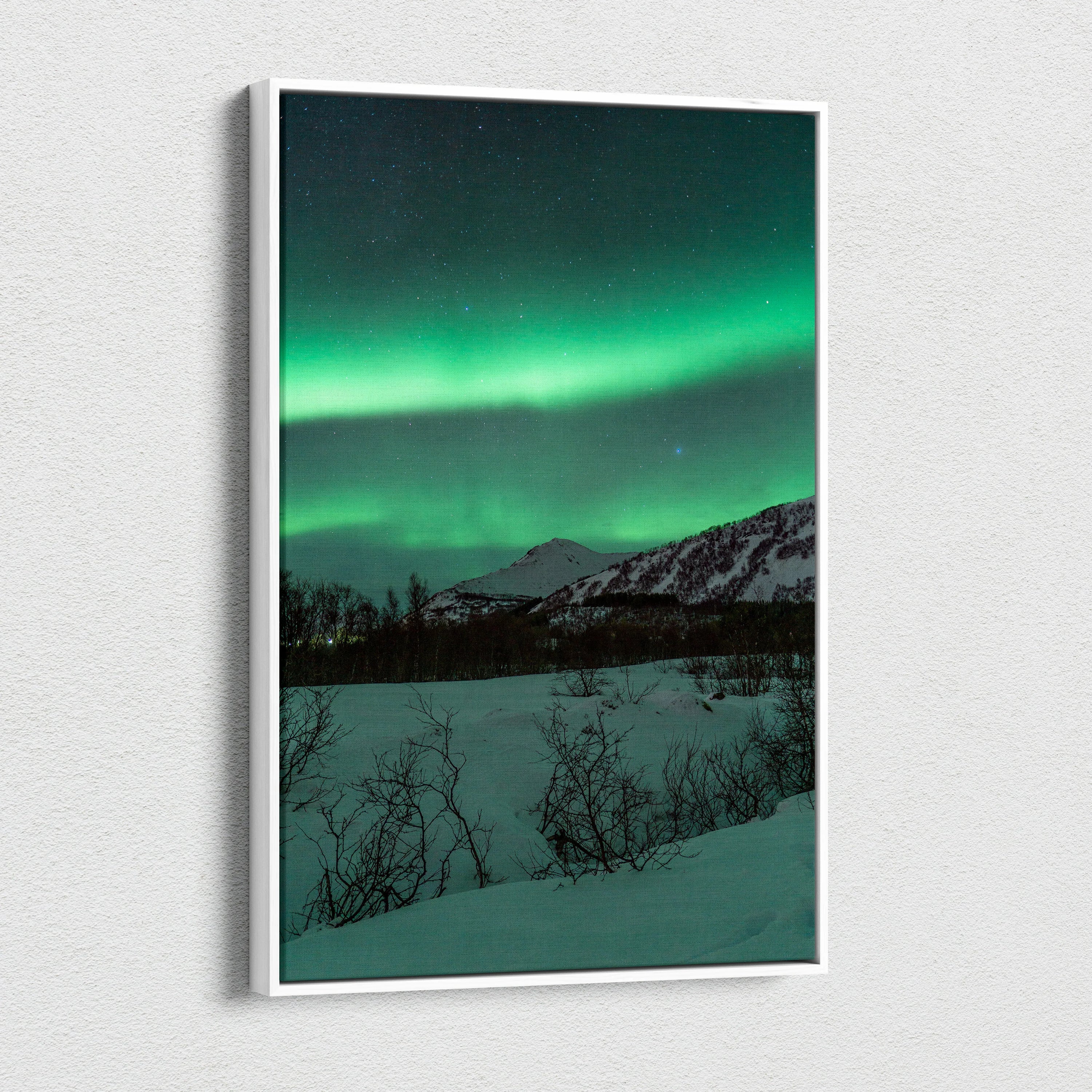 Vertical canvas wall art featuring vibrant green northern lights over snowy mountains and dark silhouetted trees.