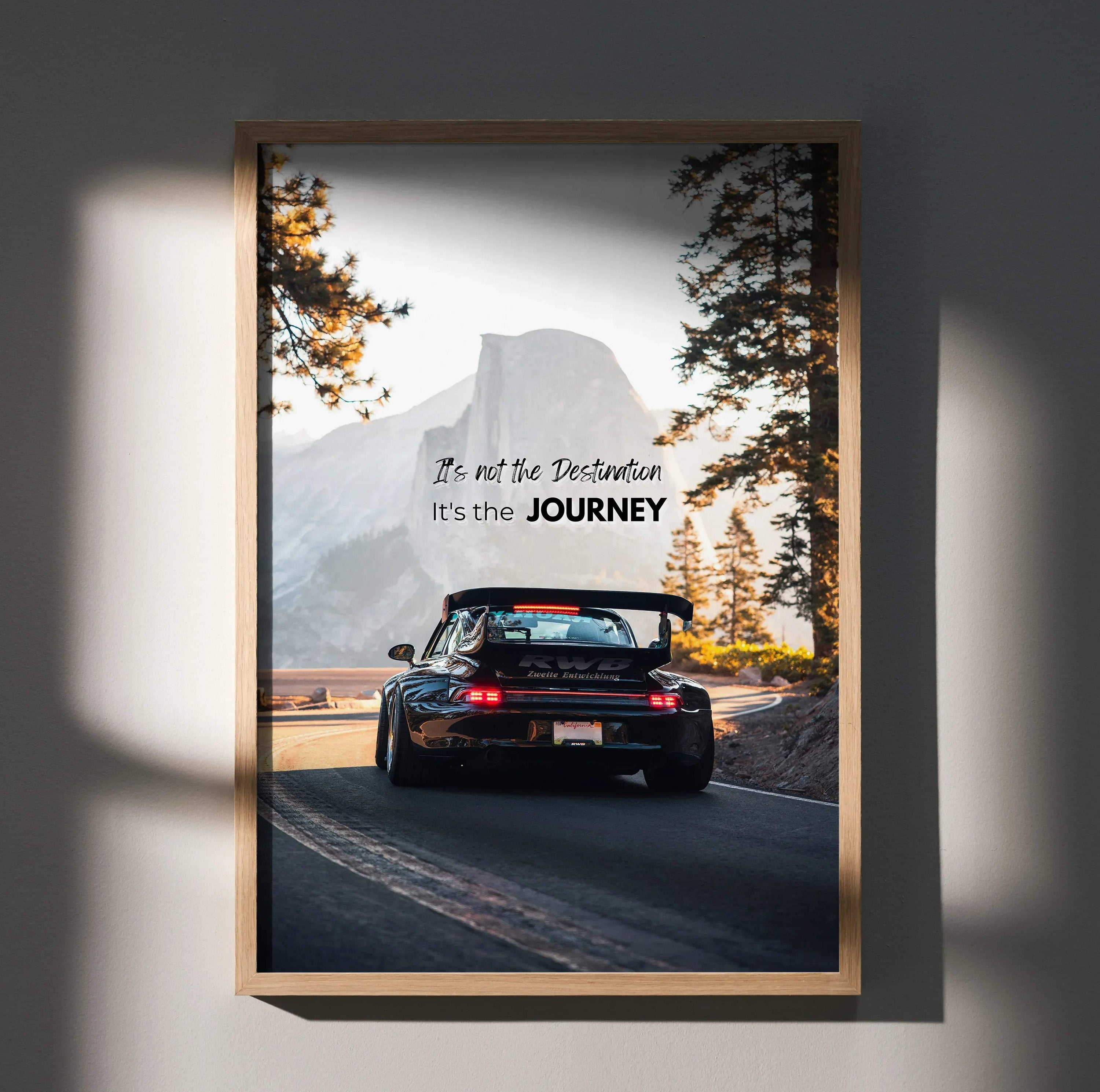 A framed motivational poster of a black porsche 911 with rear spoiler driving on a mountain road with inspiring text