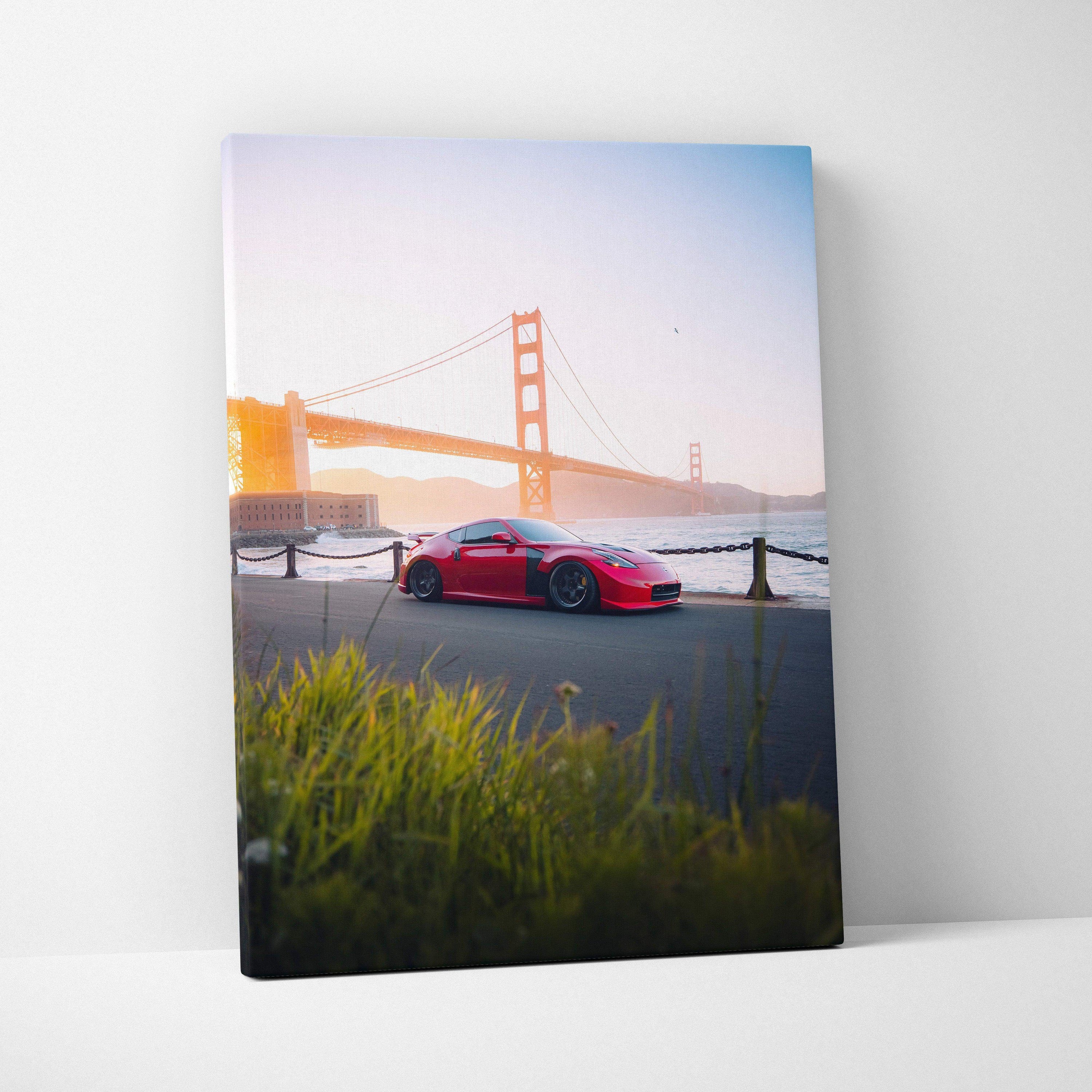 Vertical canvas wall art featuring a red Nissan 370z with Golden Gate Bridge backdrop at sunrise.