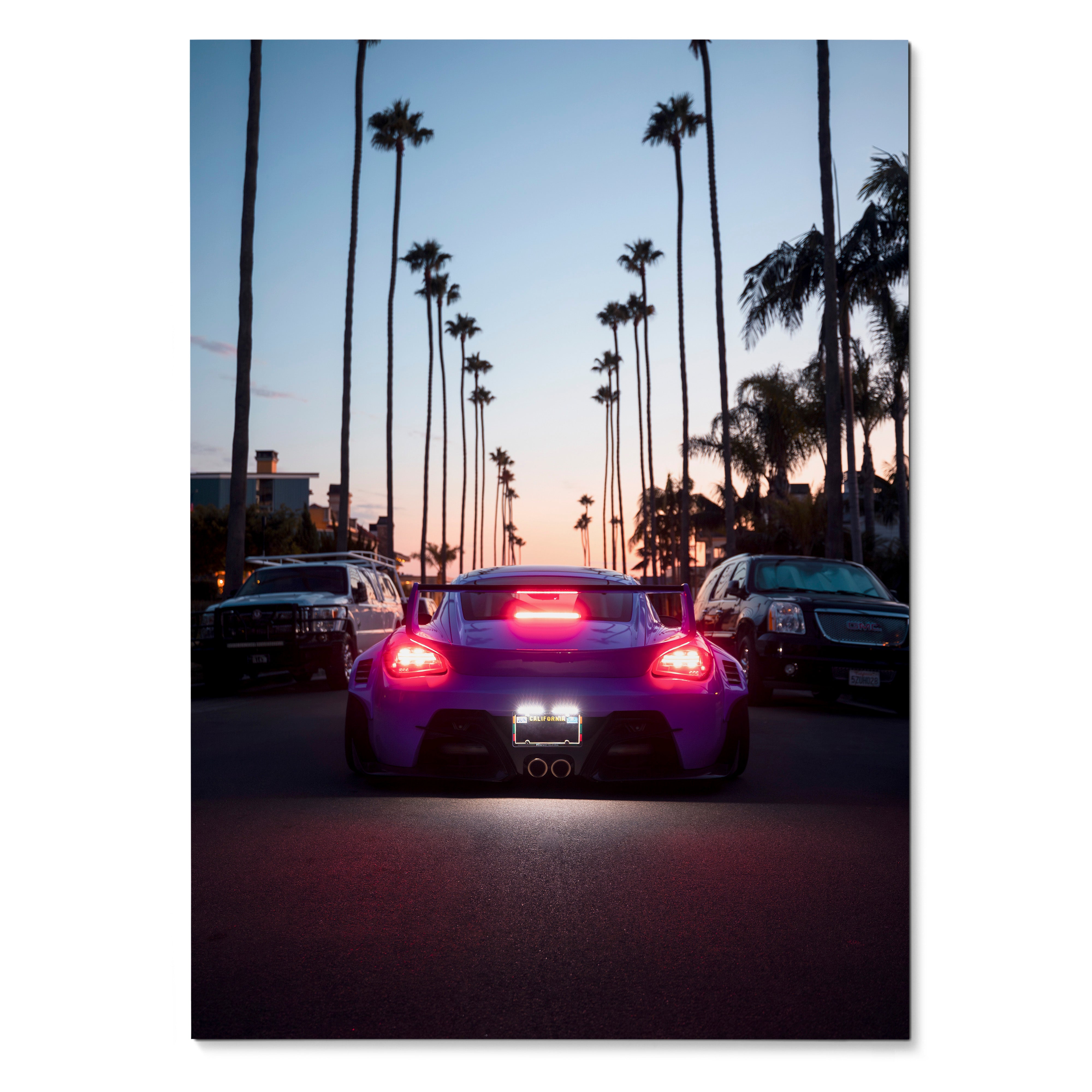 Porsche Cayman poster showing rear view of sports car with glowing red taillights on palm-lined street at dusk wall art.