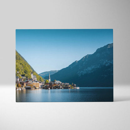 Canvas wall art featuring a serene lakeside village with colorful buildings and a church steeple, set against mountains.
