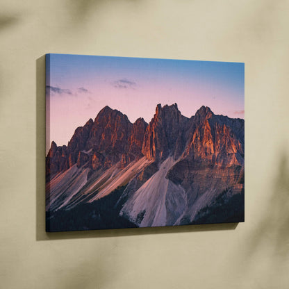 Canvas wall art featuring rugged mountain peaks bathed in warm sunset hues against a soft blue sky.