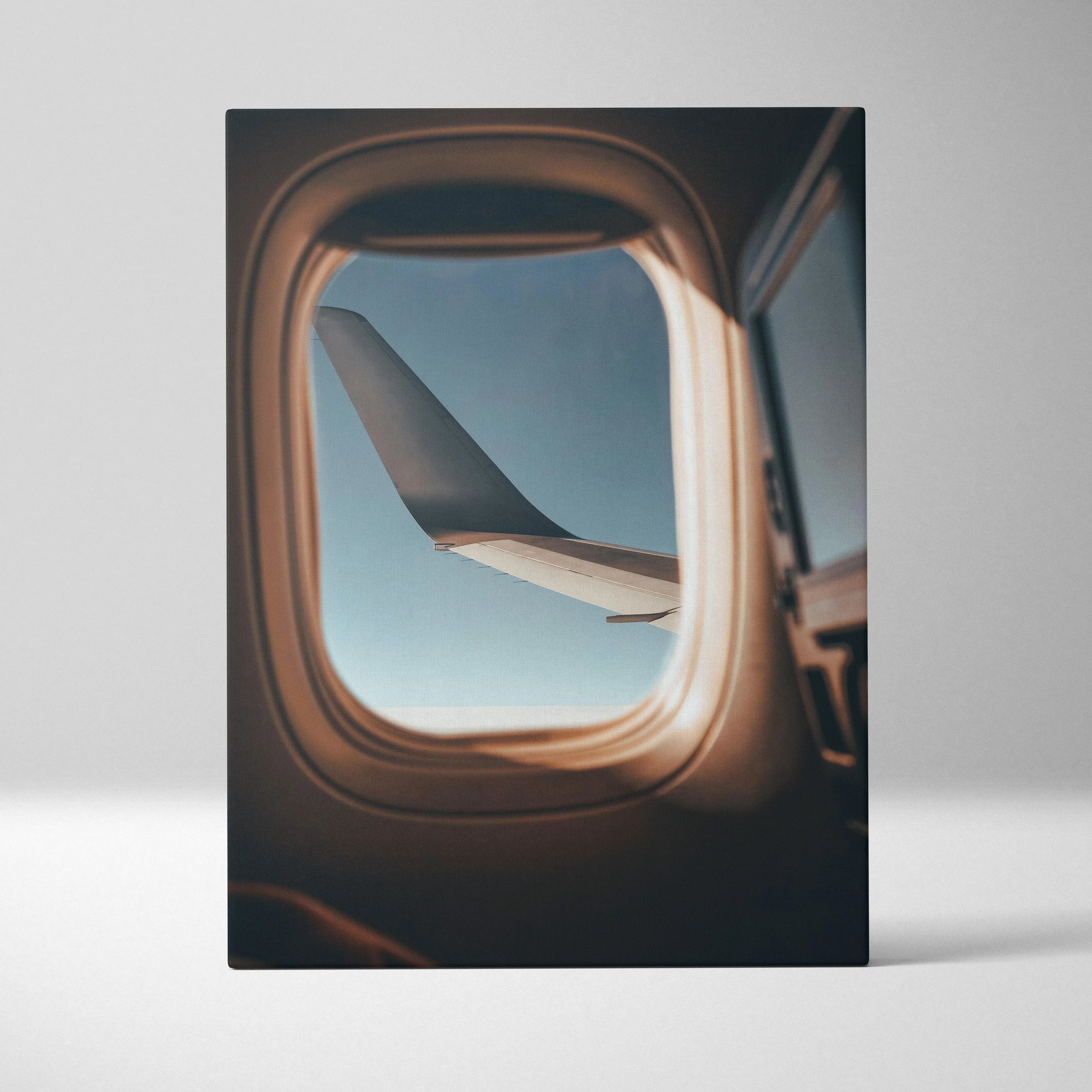 Vertical canvas wall art of airplane wing framed by window, soft light and blue sky visible outside.