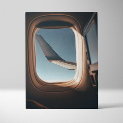 Vertical canvas wall art of airplane wing framed by window, soft light and blue sky visible outside.