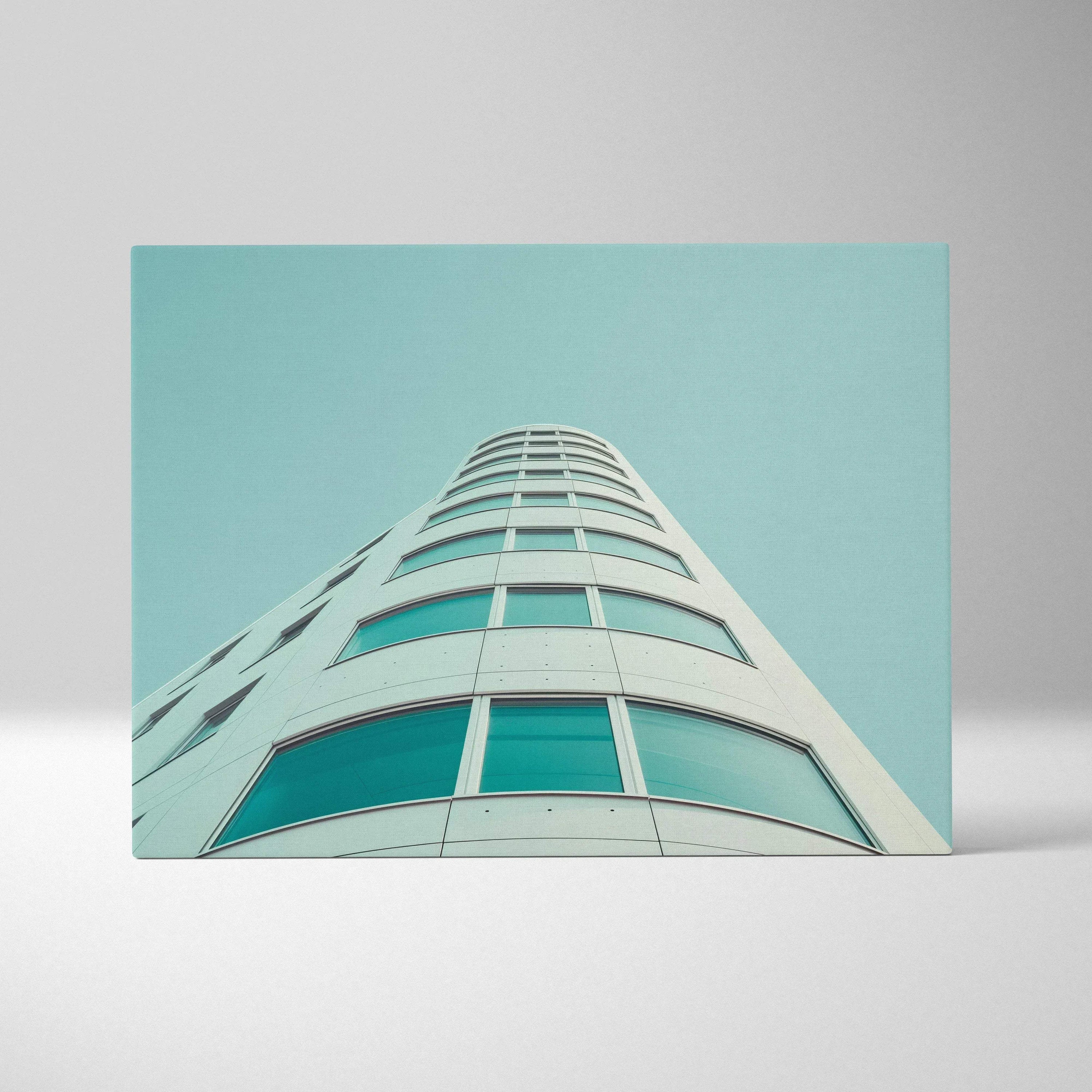 Curved modern building with glass windows in blue tones on canvas wall art with teal sky background.