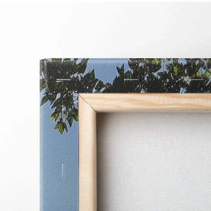 Canvas wall art with a corner of natural wood frame and a blue sky with green foliage design.