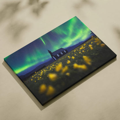 Canvas print of black wooden church under aurora borealis in wildflower field