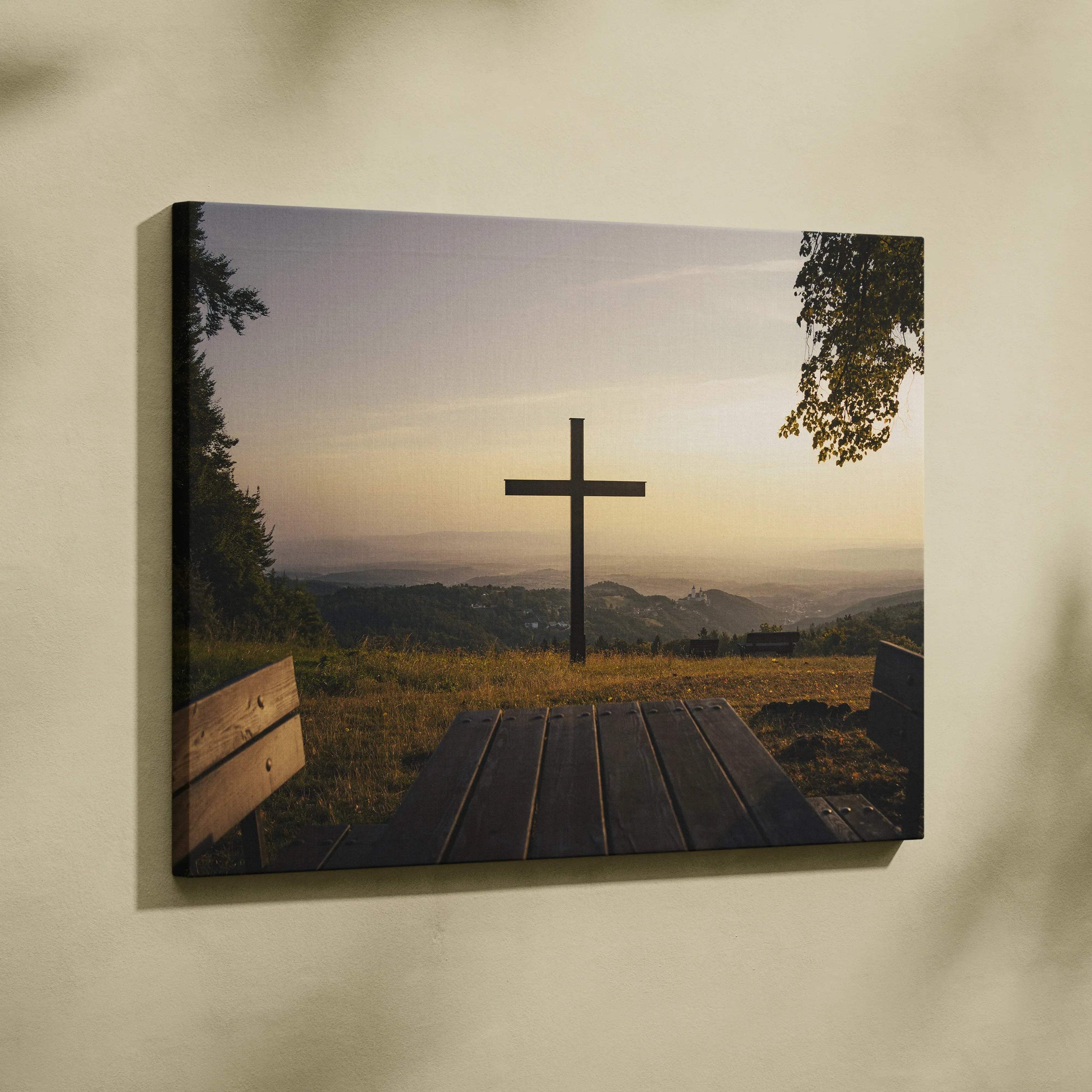 Canvas wall art featuring a silhouetted cross at sunset over a peaceful nature landscape with distant hills.