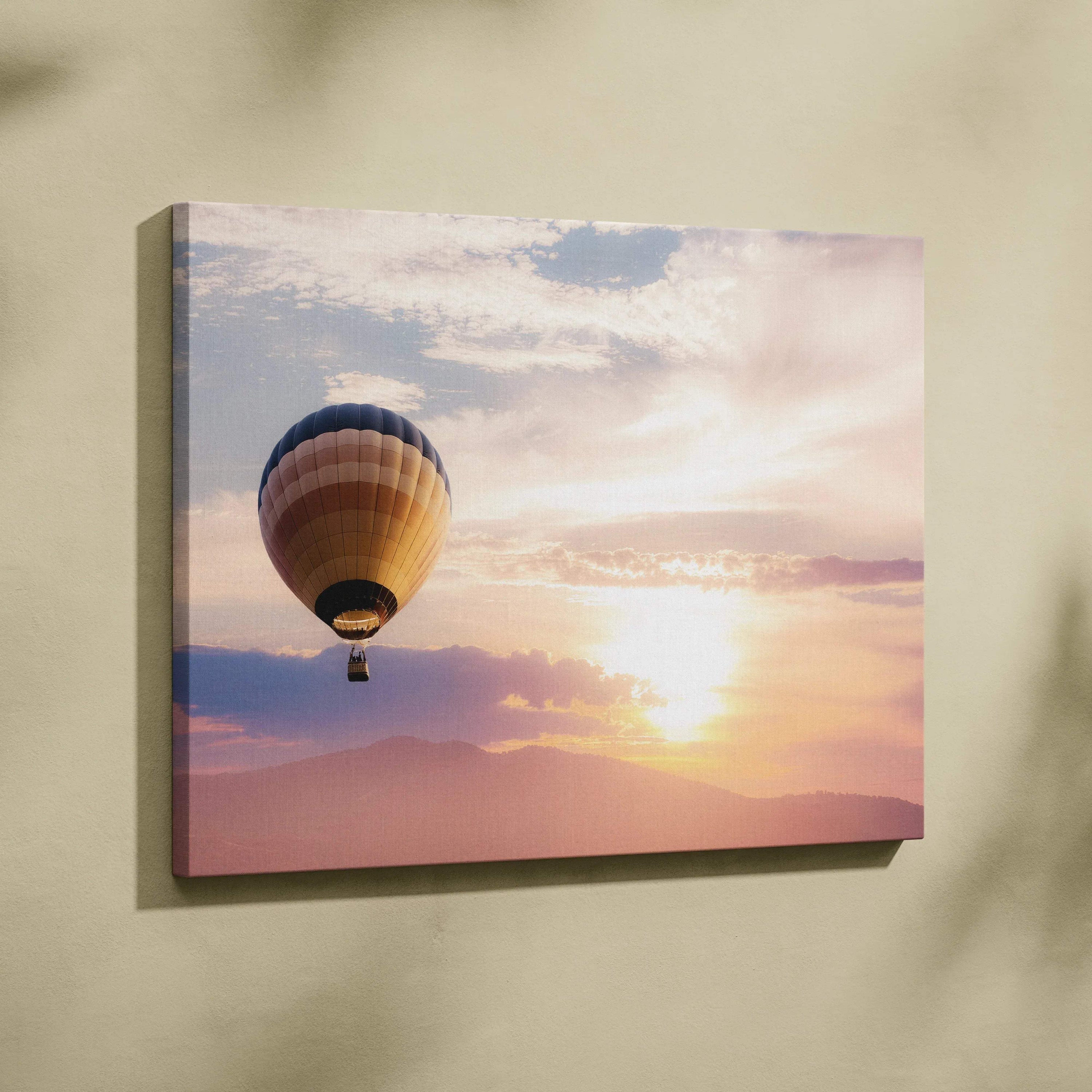 A rectangular canvas print of a hot air balloon with blue tan and gold stripes against a warm peach and orange sunset glow