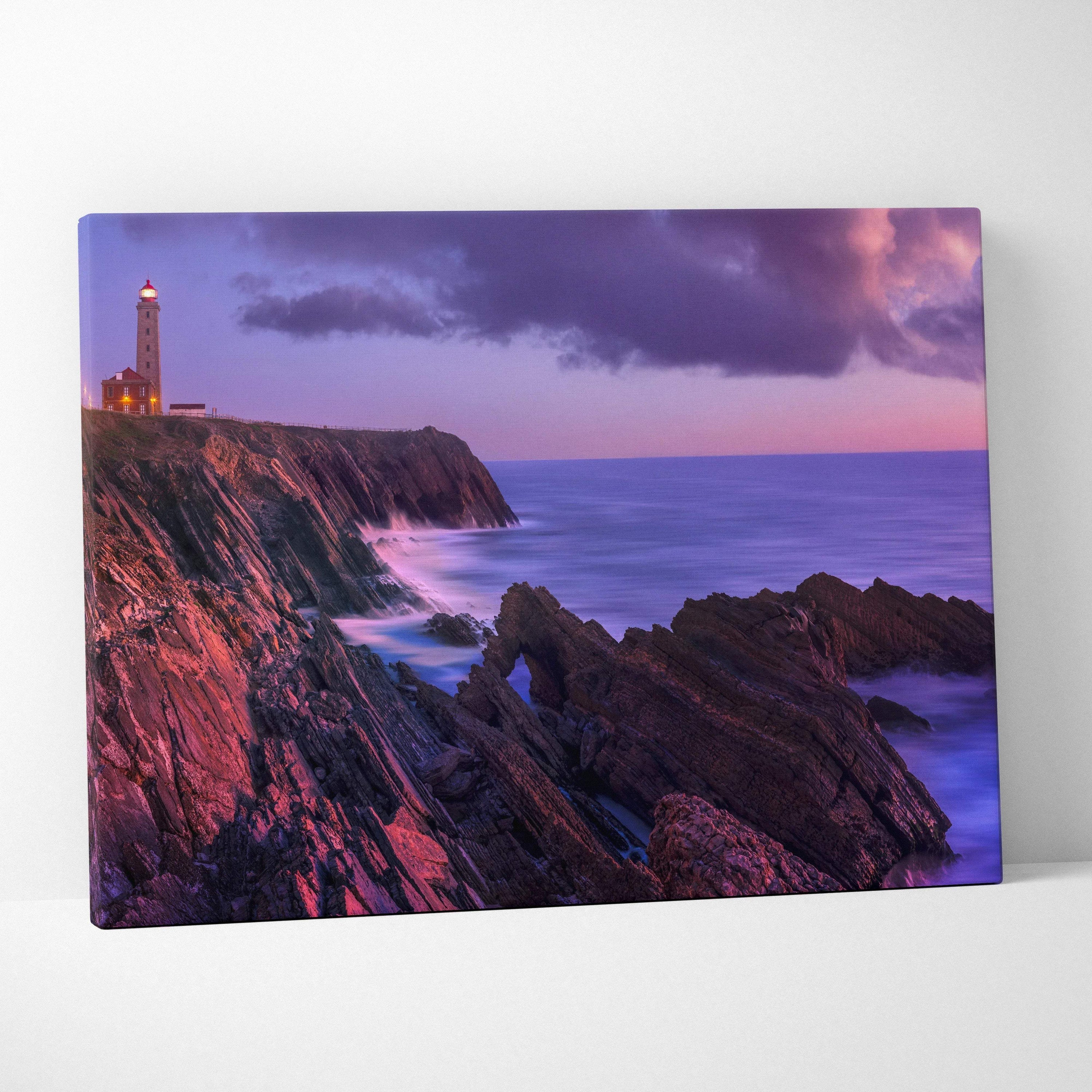 Canvas wall art featuring a tranquil beach sunset with rocky cliffs and a lighthouse under purple skies.