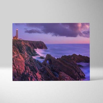 Canvas wall art featuring a serene sunset beach with a lighthouse on rocky cliffs under a purple sky.
