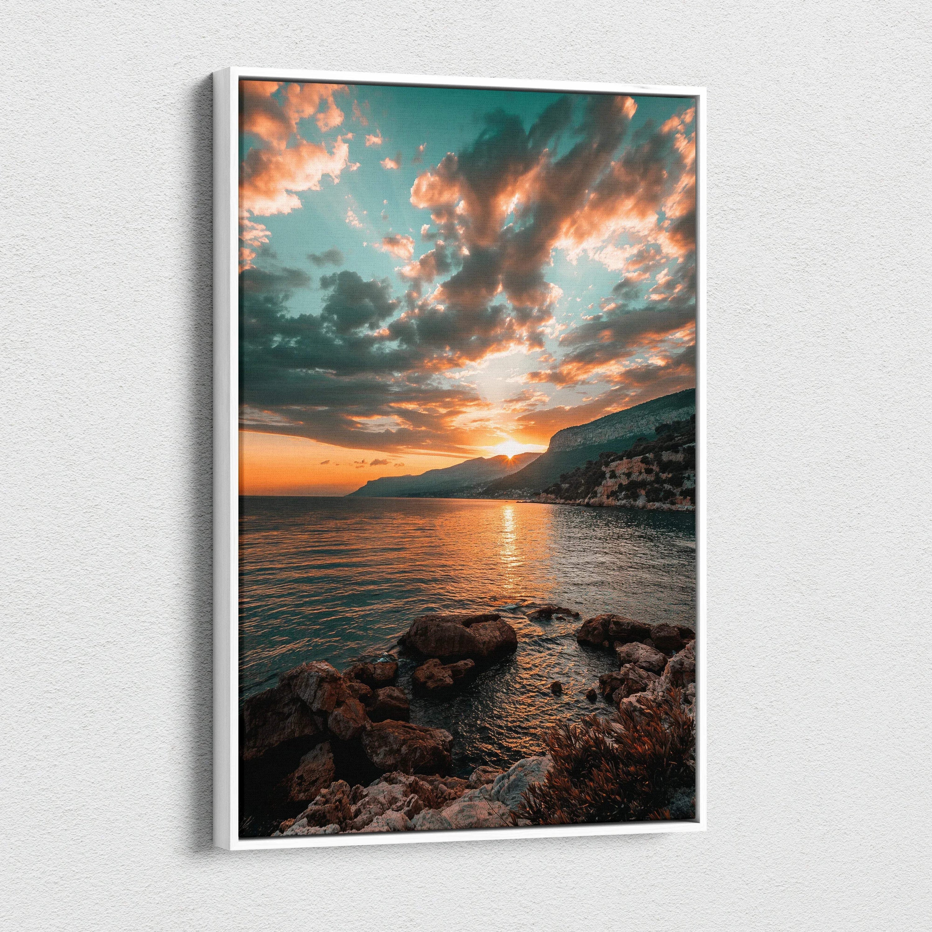 Vertical canvas wall art featuring a colorful sunset over mountains and rocky shoreline.