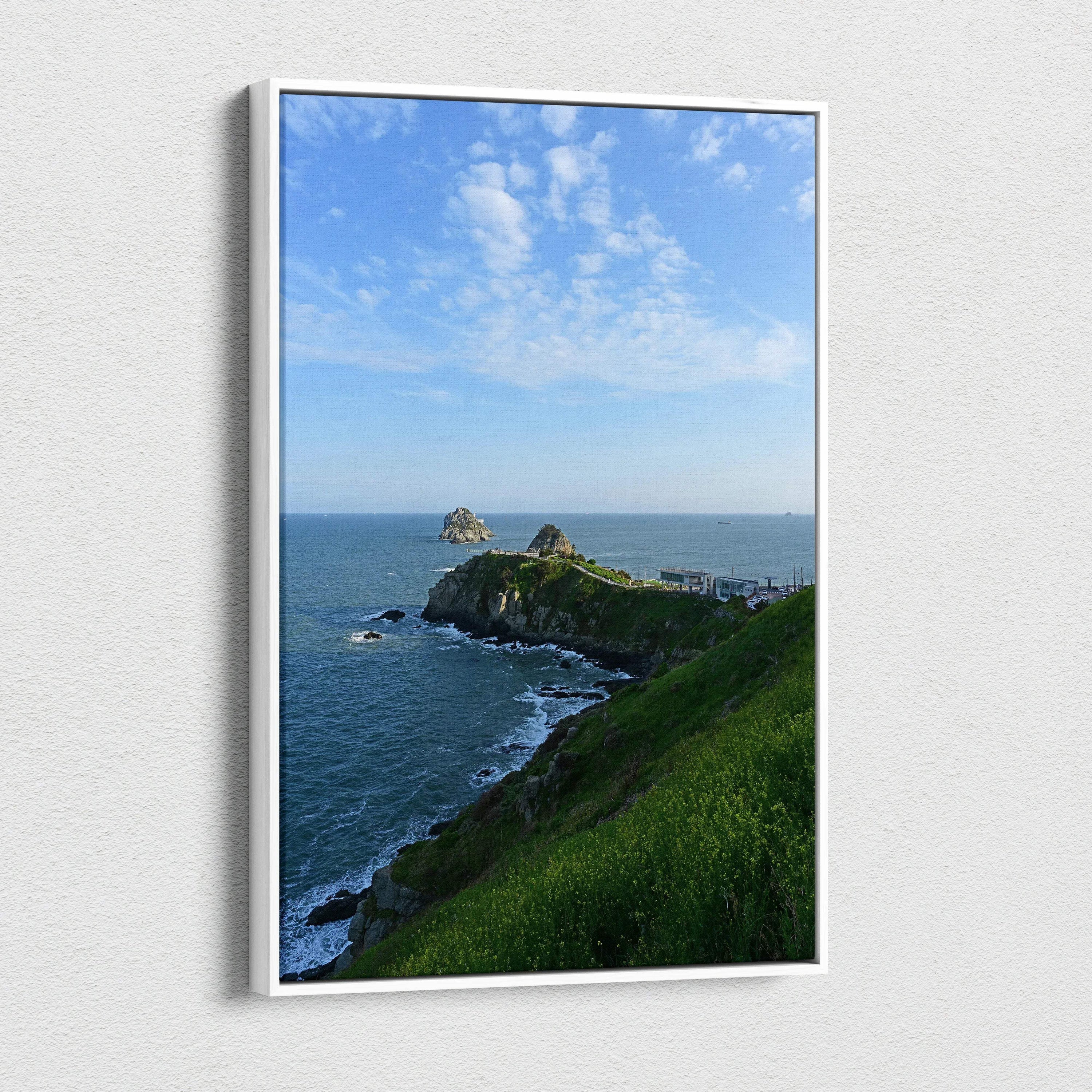 Vertical canvas wall art of green cliffside overlooking blue ocean under a bright sky with wispy clouds.