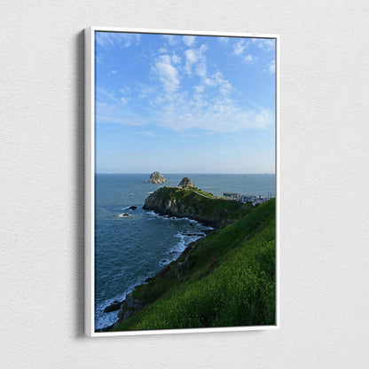 Vertical canvas wall art of green cliffside overlooking blue ocean under a bright sky with wispy clouds.
