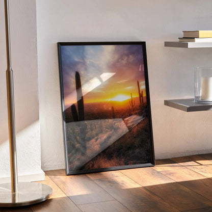 Desert sunset wall art poster with vibrant orange sky and silhouettes of tall cacti in black frame.