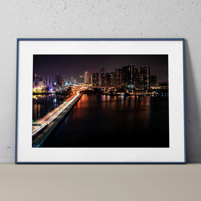 Vibrant city night skyline wall art poster with illuminated buildings and reflections on water.