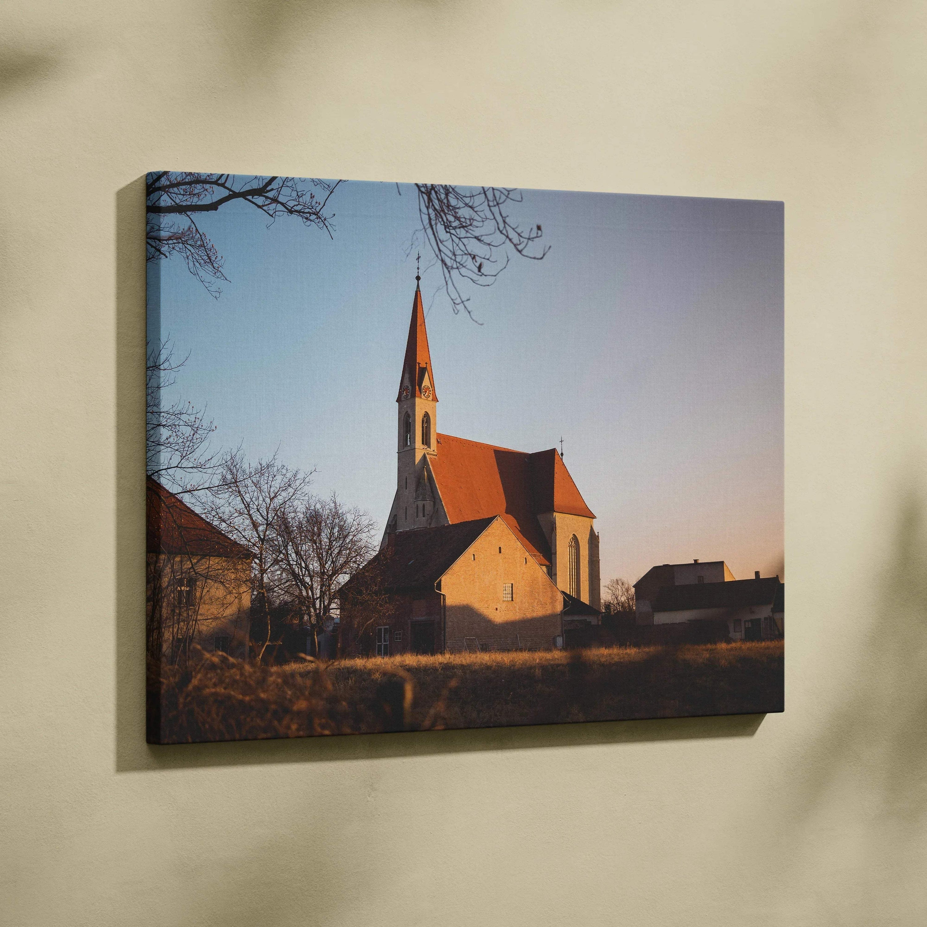 Canvas wall art of a church building with a tall steeple at sunset, warm lighting and soft shadows.
