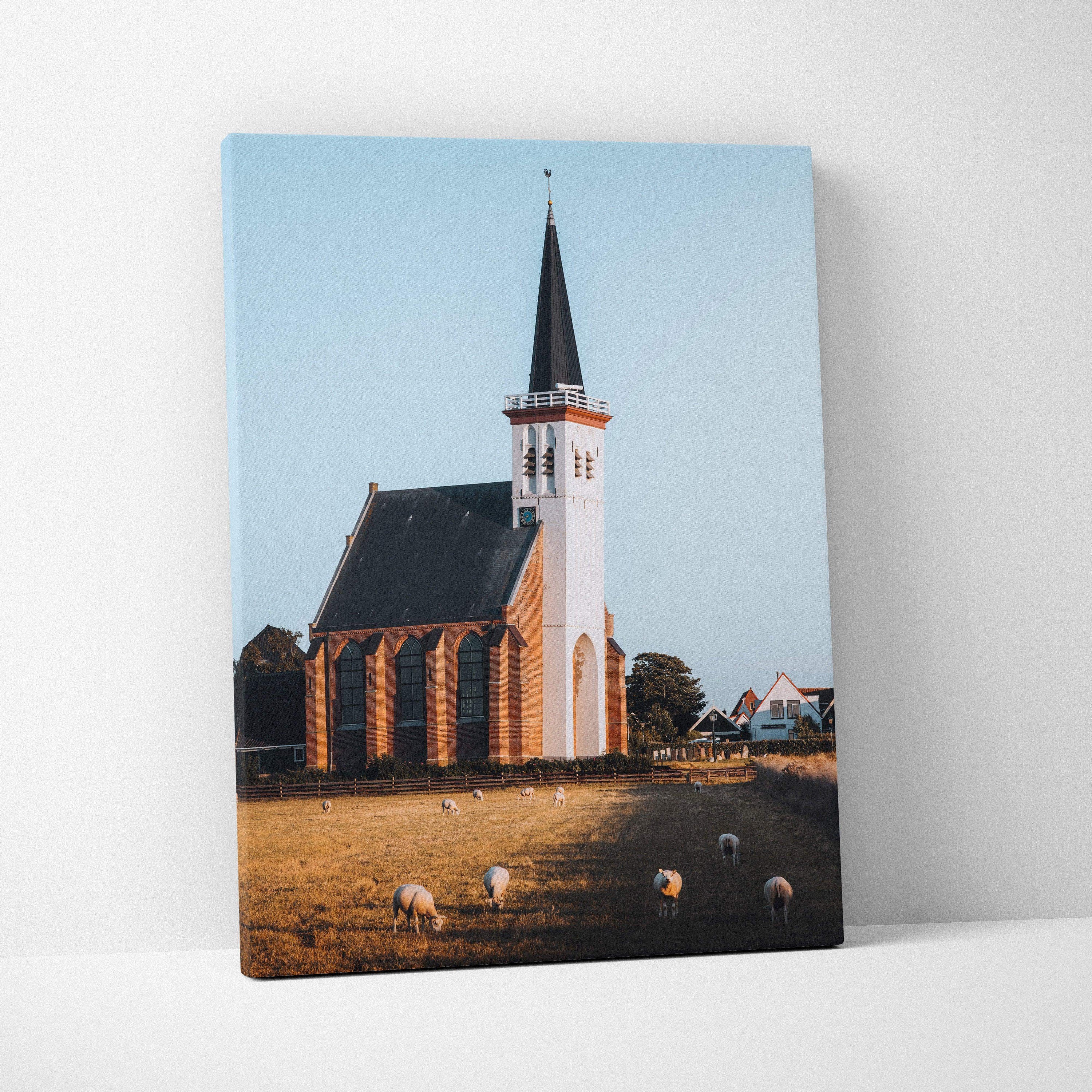 Canvas wall art featuring a tall church with spire against a clear blue sky and grazing sheep.