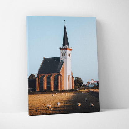 Canvas wall art featuring a tall church with spire against a clear blue sky and grazing sheep.