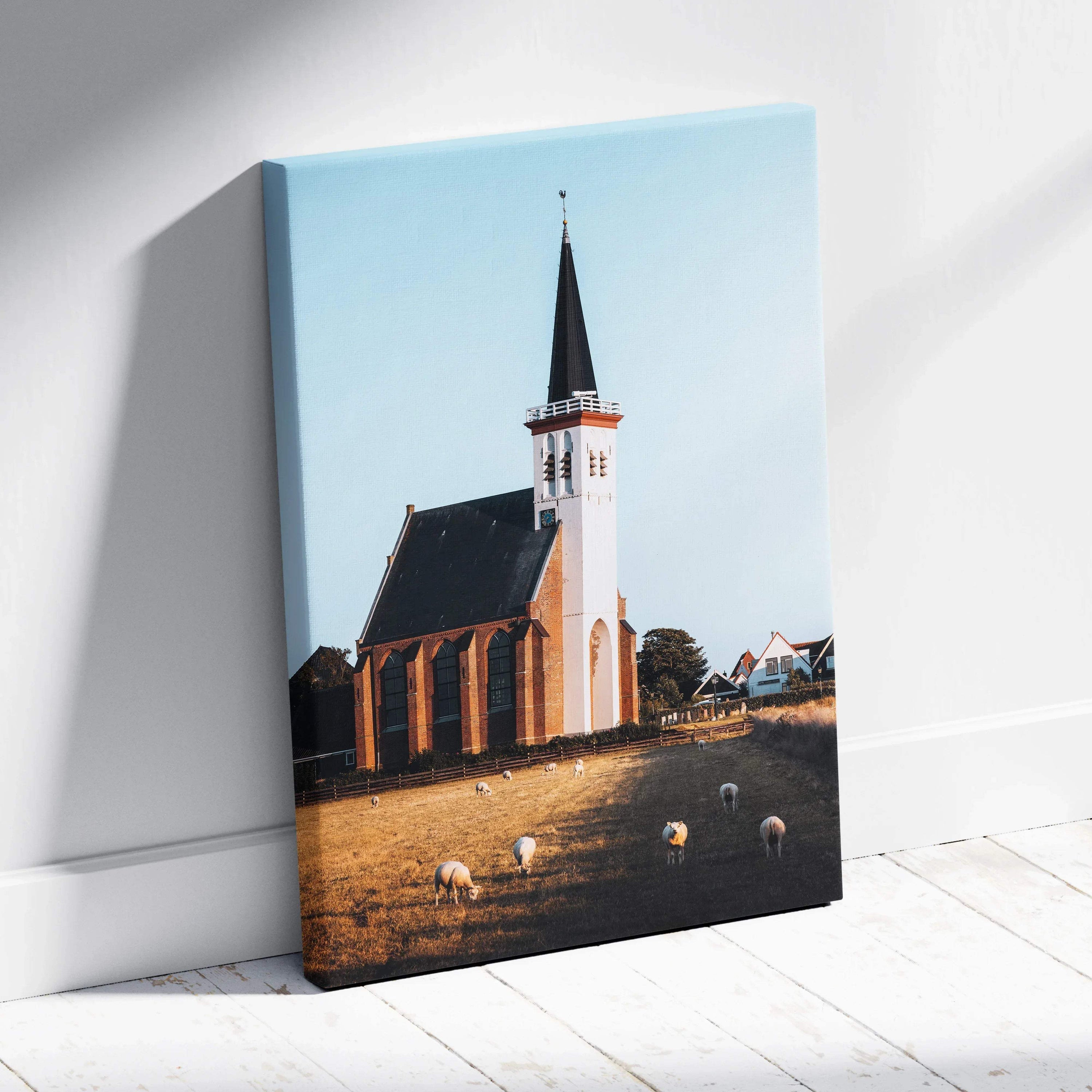 Canvas wall art of a tall white church with a steeple against a clear blue sky and sheep grazing in front.