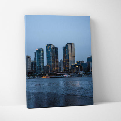 Vertical canvas wall art featuring a vibrant urban cityscape with illuminated buildings at dusk.