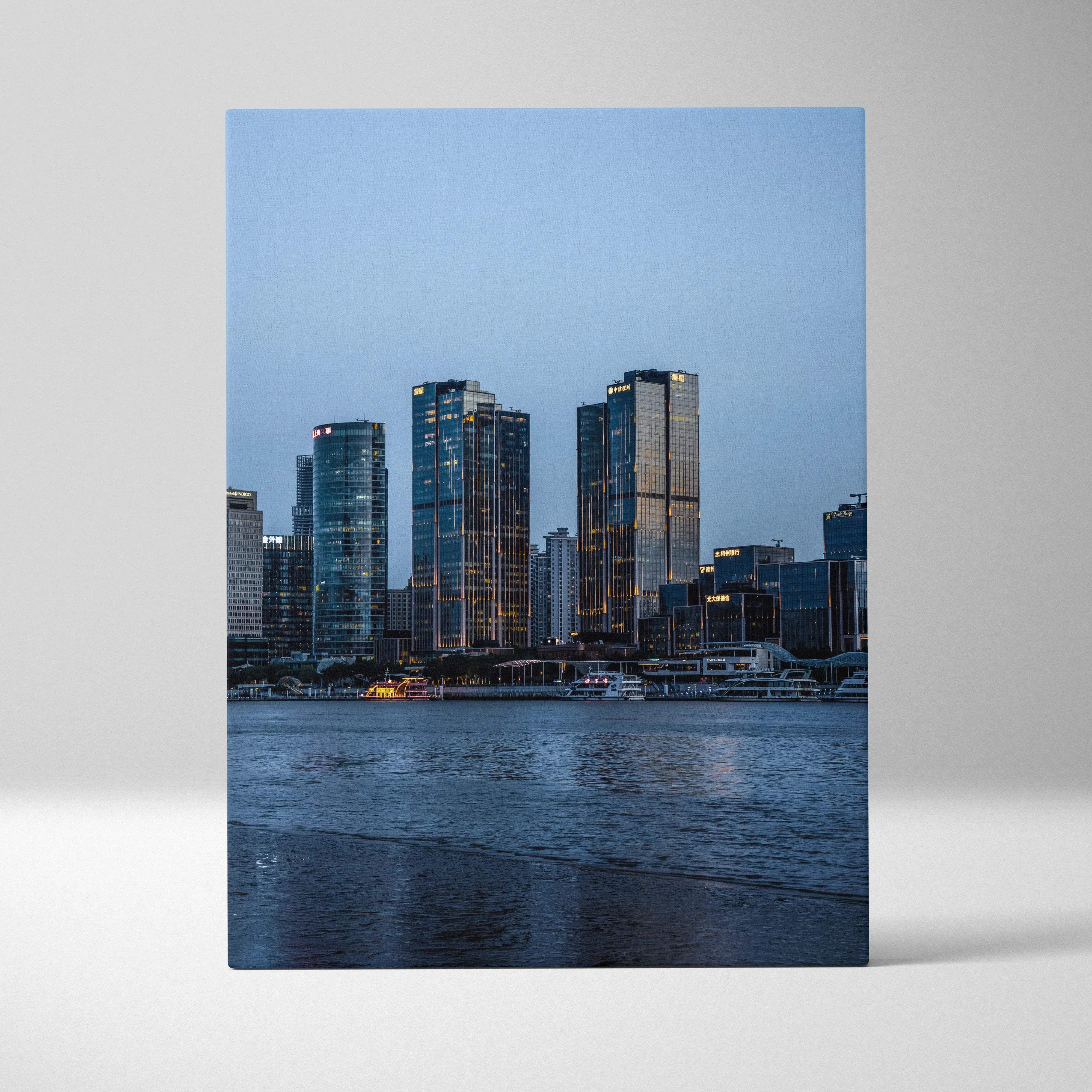 Canvas print of a modern city skyline at dusk with illuminated glass skyscrapers reflected in calm water
