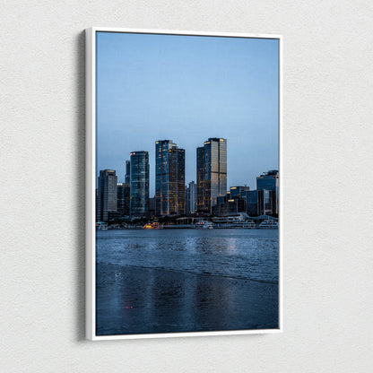 Vertical canvas wall art featuring a vibrant cityscape with tall buildings at dusk.