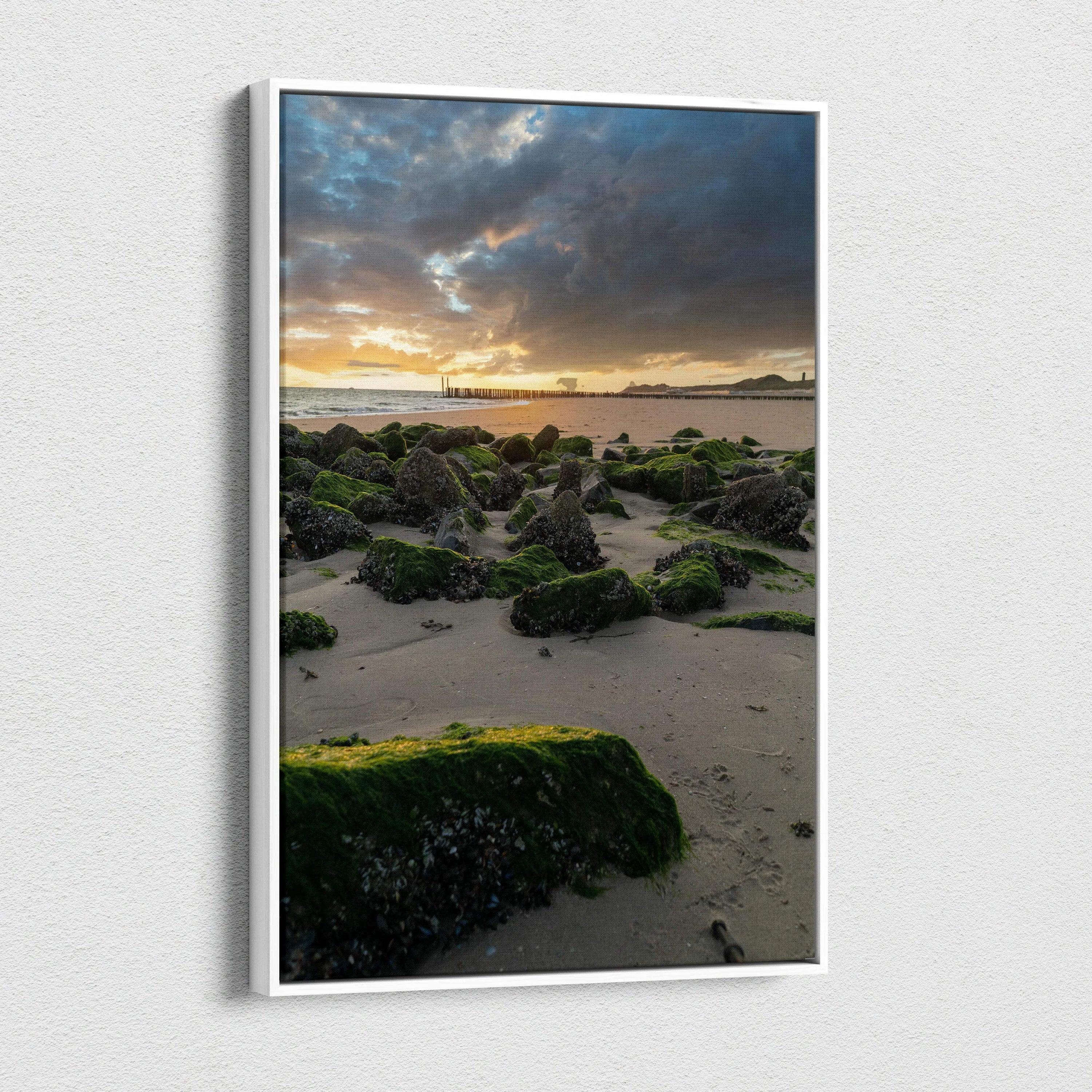 Canvas wall art of serene beach at sunset with moss-covered rocks and dramatic clouds.