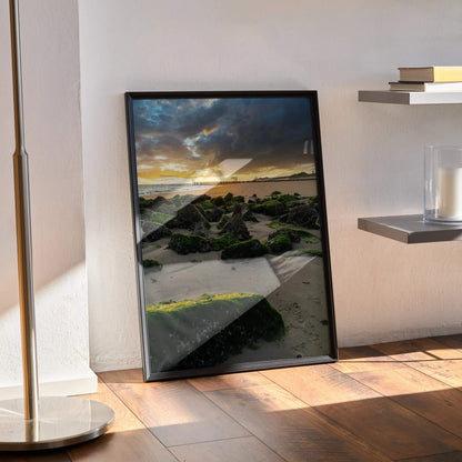 Vertical wall art poster featuring a tranquil ocean sunset with moss-covered rocks and dramatic clouds.