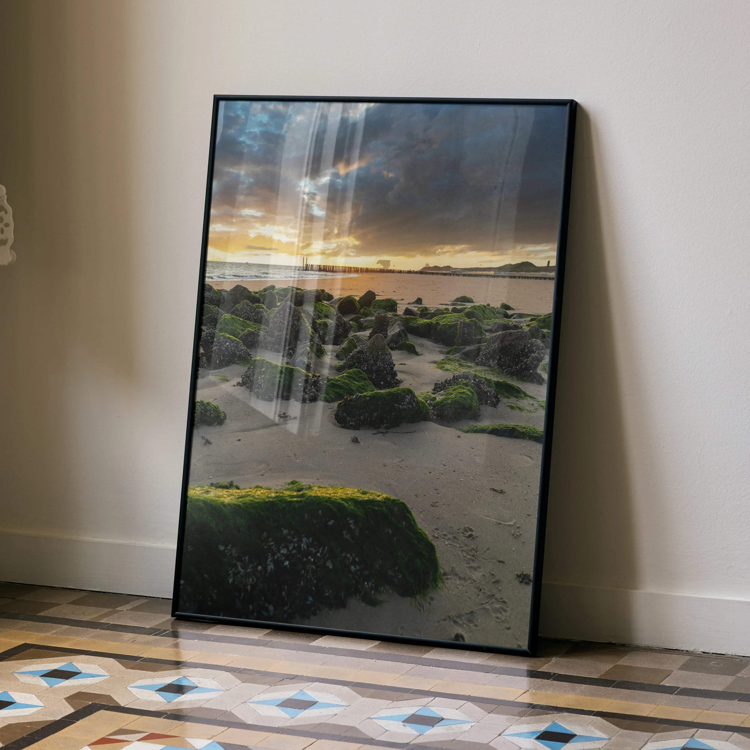 Tranquil ocean sunset wall art poster with moss-covered rocks on sandy beach in vertical frame.