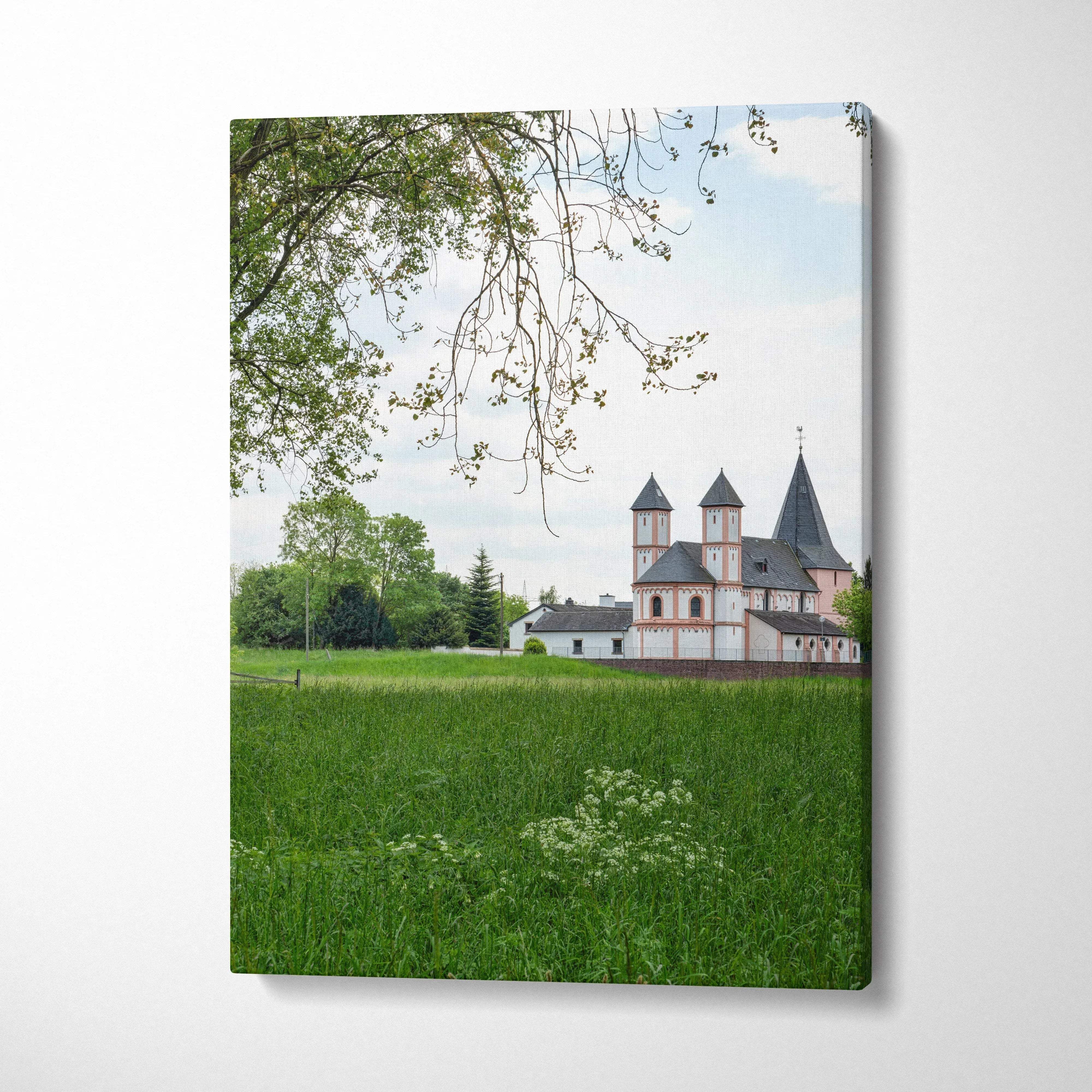 Canvas wall art featuring a rural building with towers framed by green fields and tree branches.