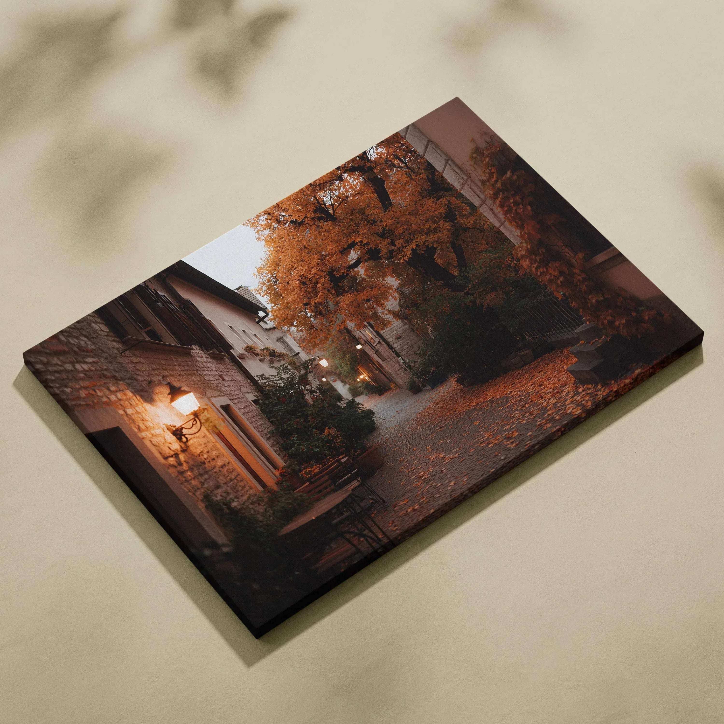 Canvas wall art featuring a serene autumn pathway with orange leaves and rustic buildings at dusk.