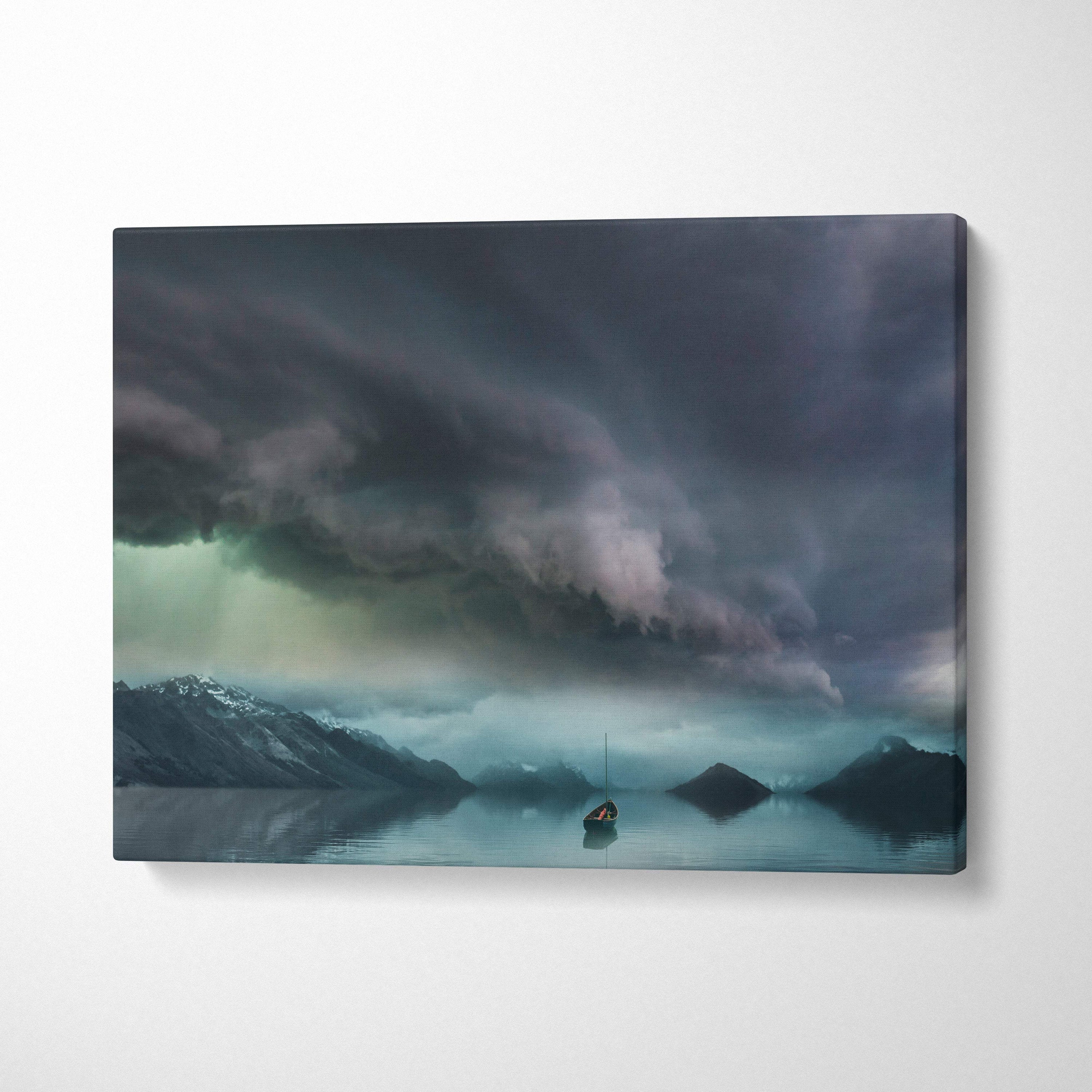 Rectangular canvas print of a moody sky with dark stormy clouds over snow-capped mountains and a lone sailboat on calm water