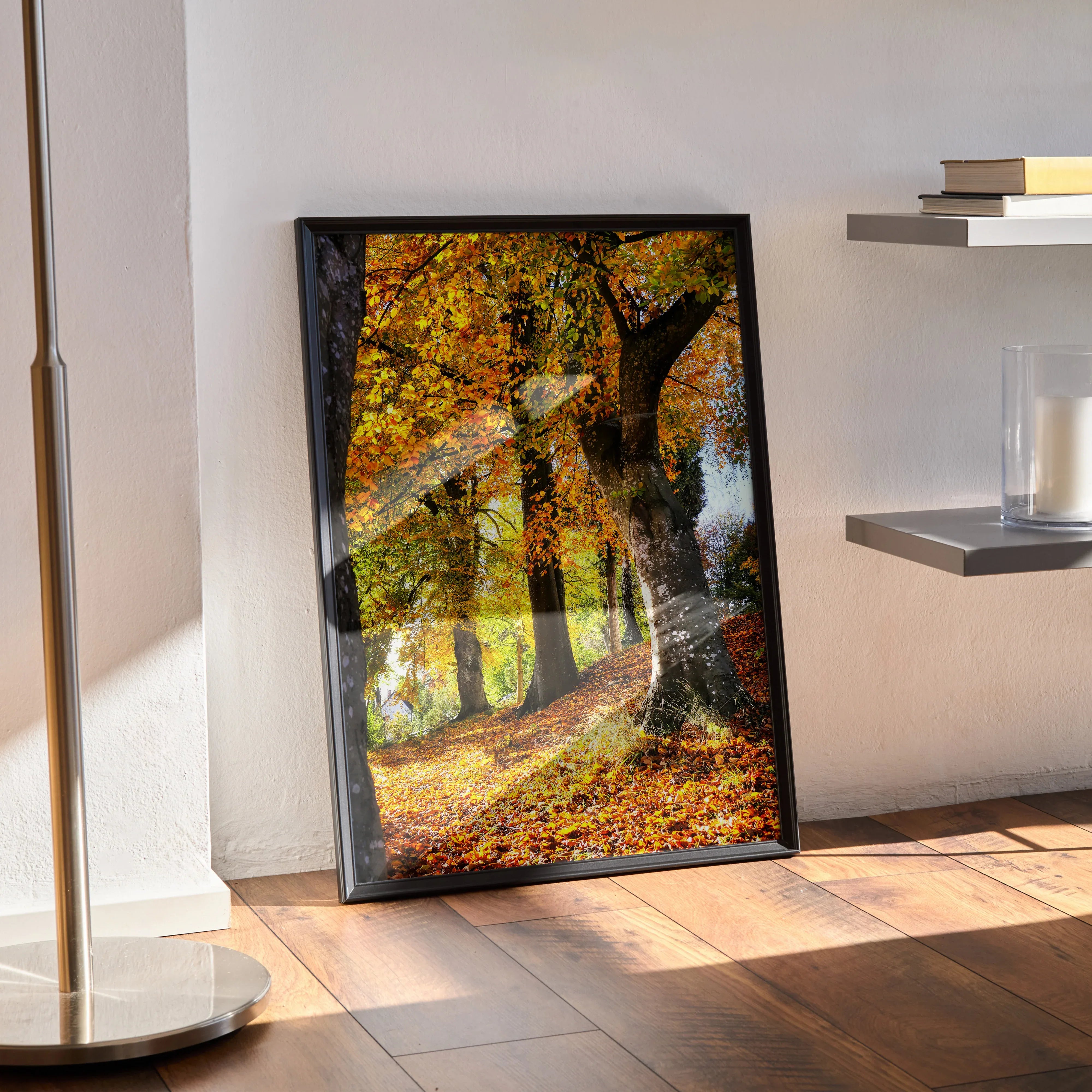 Serene autumn forest wall art poster with golden leaves and tree trunks in vertical black frame on wooden floor.