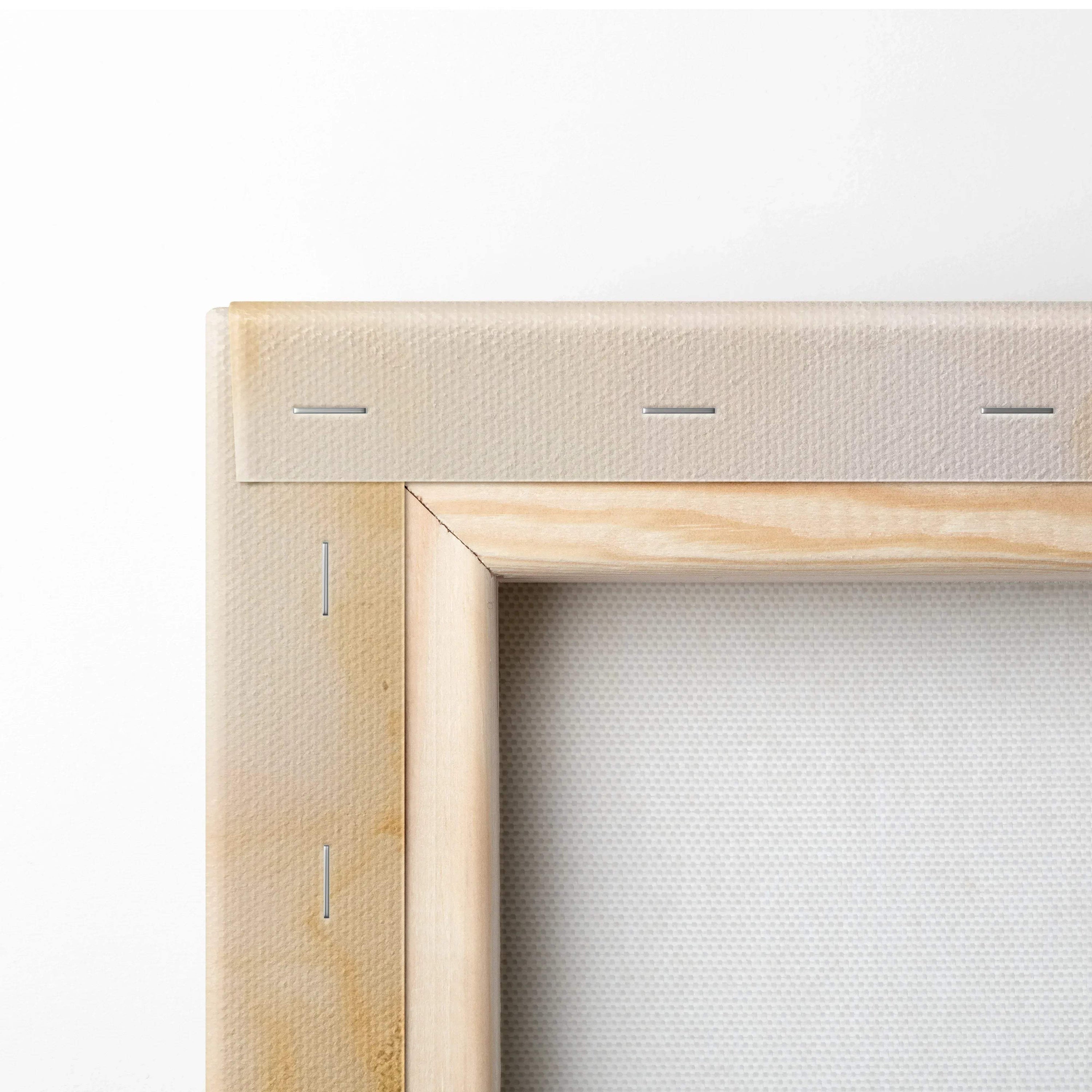 Close-up of corner of stretched white canvas on a light wooden frame with visible staples and natural wood grain.