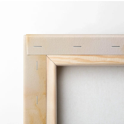 Close-up of corner of stretched white canvas on a light wooden frame with visible staples and natural wood grain.
