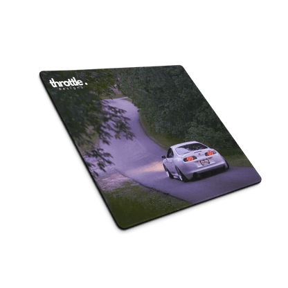 Gaming mouse pad featuring a rear view of a white Toyota Supra Mk4 driving on a winding tree-lined road at dusk.