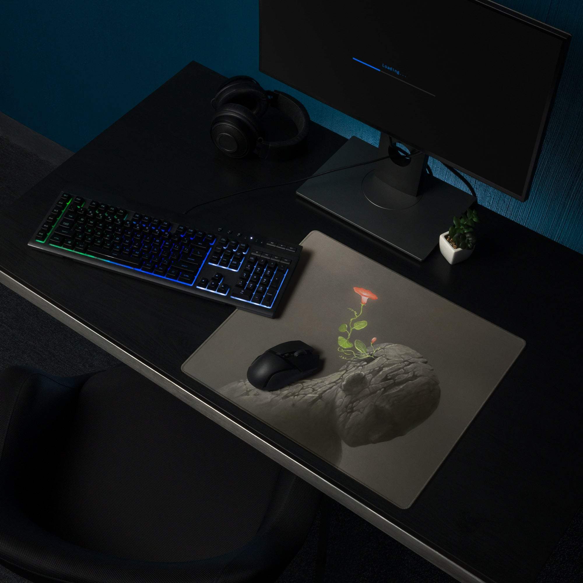 A sleek charcoal gray rock flower desk pad featuring a 3d printed pink flower blooming from textured stone